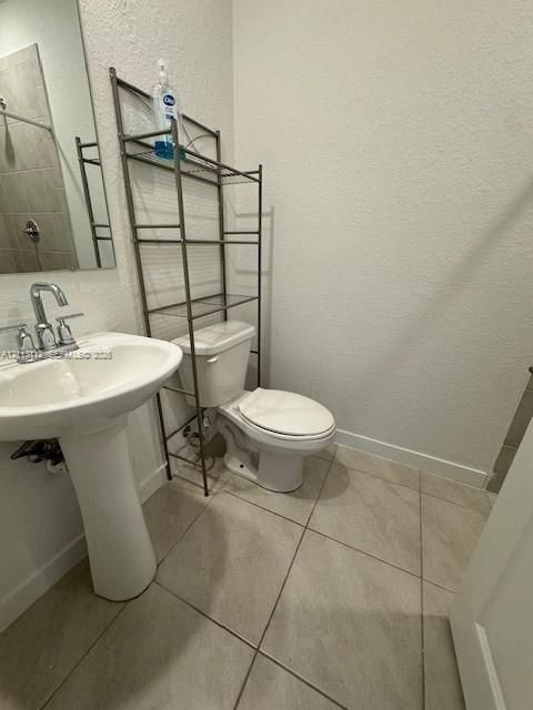 Pedestal sink with a dual-handle chrome faucet, large rectangular mirror, and neutral-toned floor tiling