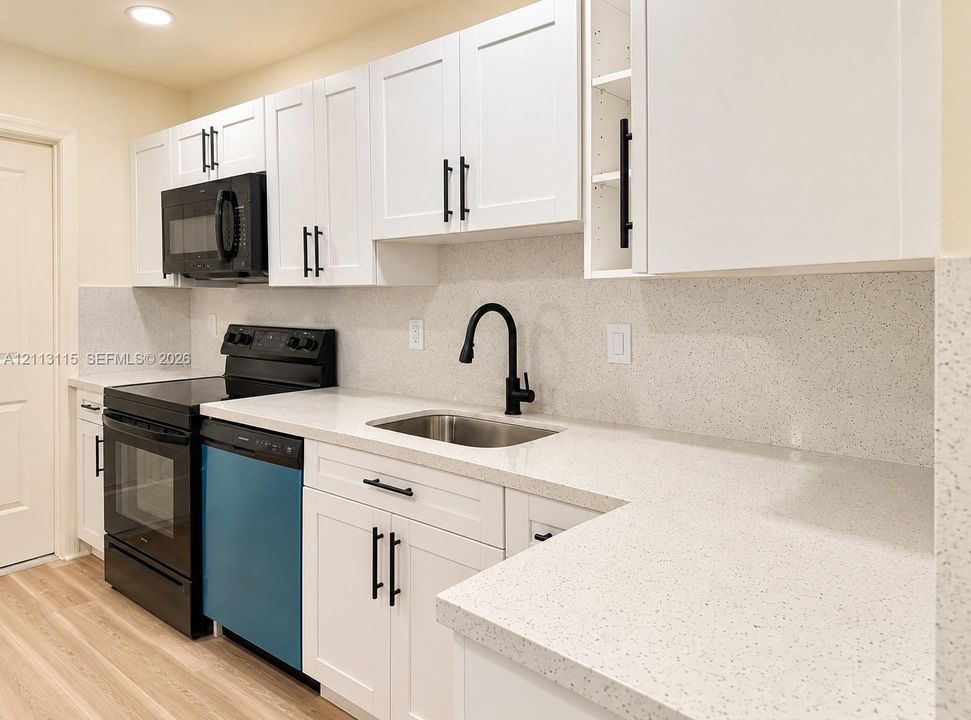 Kitchen featuring shaker-style white cabinetry, light-toned composite countertops, a stainless steel undermount sink with a matte black high-arch faucet, and black appliance package