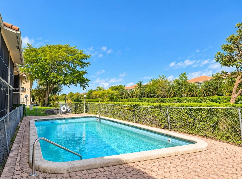 In-ground swimming pool featuring a concrete deck, metal handrail, chain-link perimeter fencing, and mature landscaping
