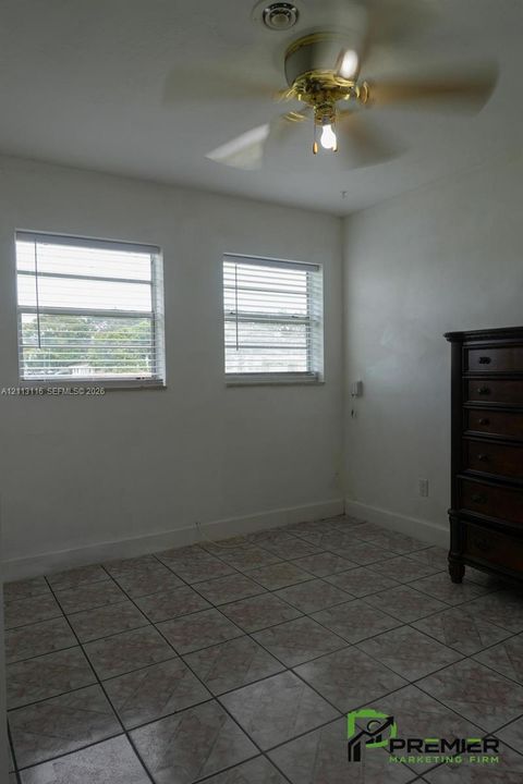 Room featuring tile flooring, dual windows with horizontal blinds, and a ceiling fan