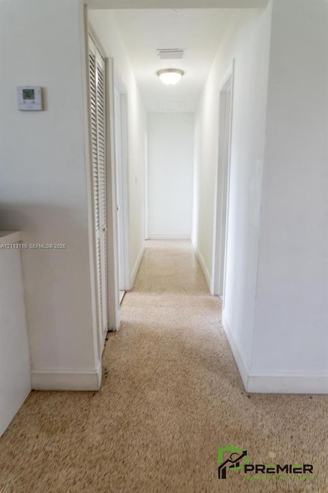 Hallway featuring neutral-toned carpeting, louvered closet doors, and a ceiling-mounted flush mount light fixture