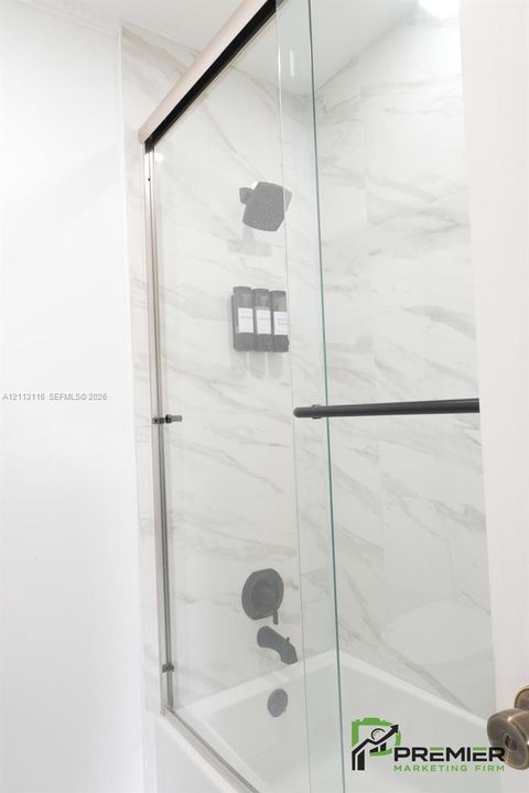 Shower enclosure featuring large-format tile surround, glass sliding door, and matte black shower fixtures