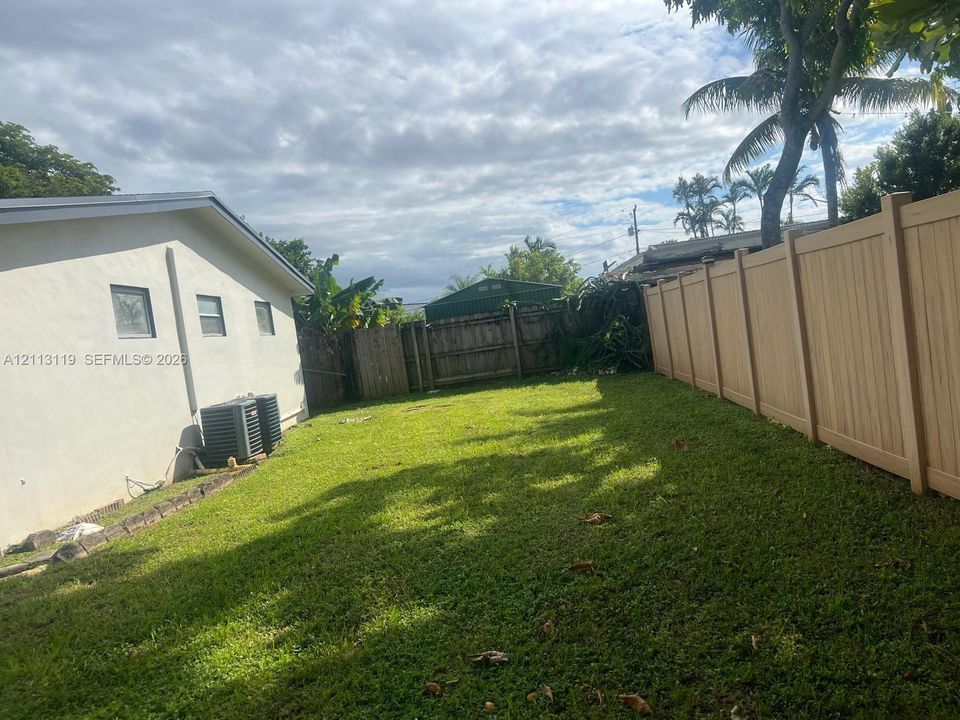 Rear yard featuring a grass lawn, perimeter vinyl fencing, and mature vegetation