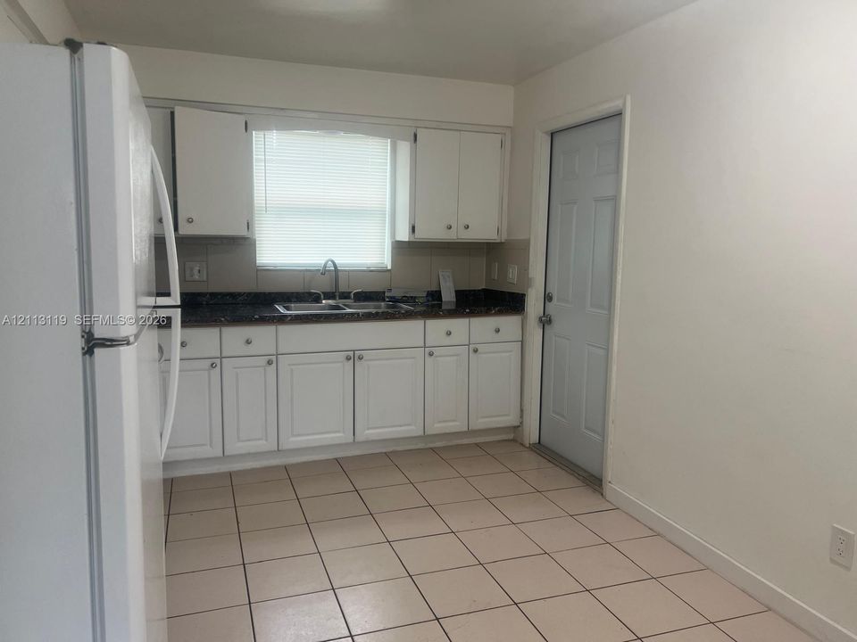 Kitchen featuring white cabinetry, dark countertops, a double-basin sink with a gooseneck faucet, tile flooring, and a six-panel exterior door