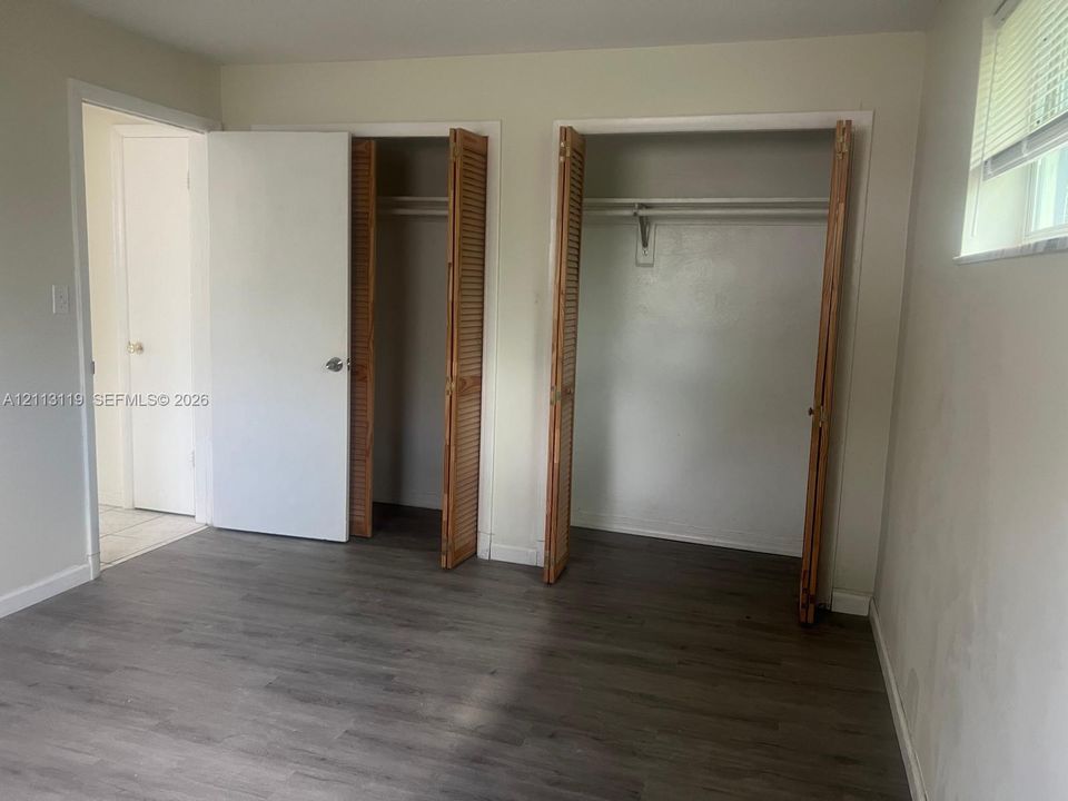 Room featuring wood-finish flooring, two dual-door closets with louvered panels, and a built-in hanging rod