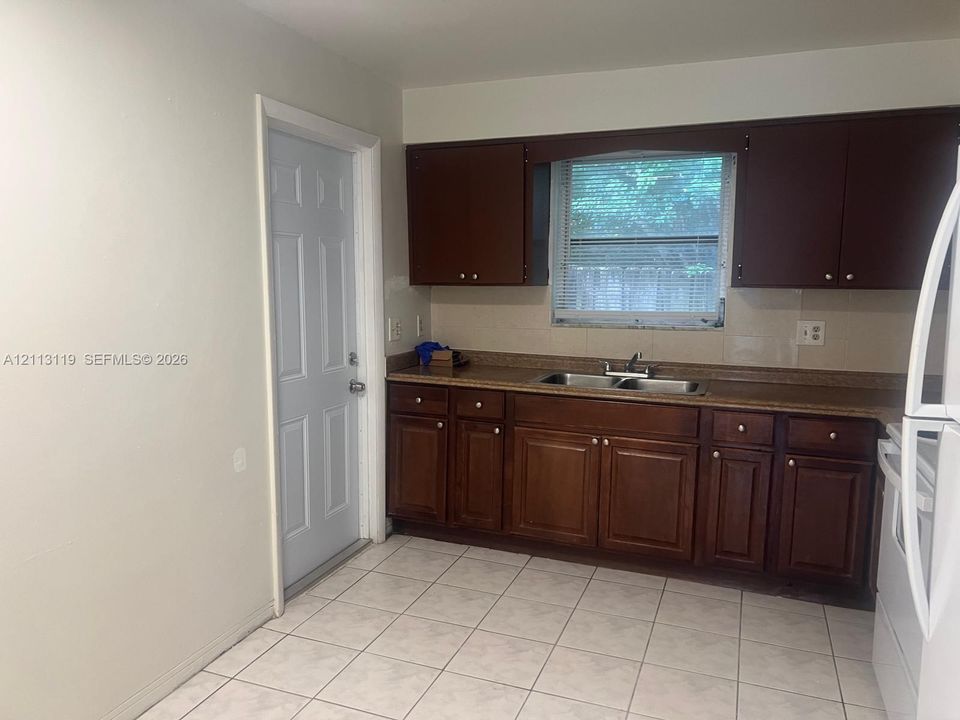 Kitchen featuring dark wood-finish cabinetry, solid-surface countertops, dual-basin stainless steel sink, and ceramic tile flooring