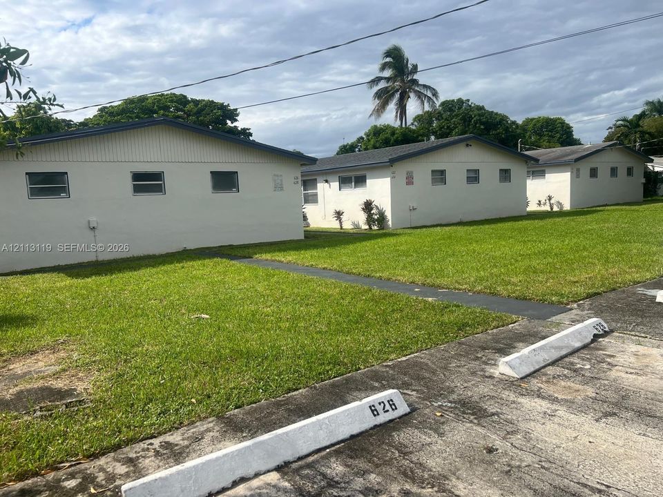 Single-story multi-unit structure featuring light-colored exterior walls, low-pitched rooflines, horizontal sliding windows, and dedicated concrete parking spaces