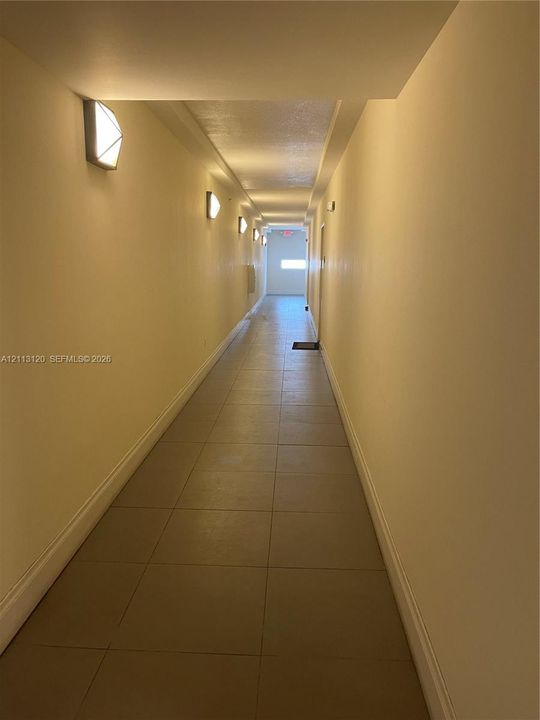 Hallway featuring large-format neutral tile flooring, smooth wall finishes, and geometric wall-mounted lighting fixtures