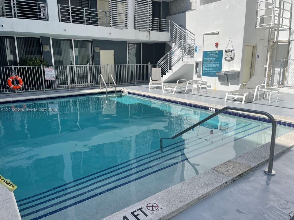 In-ground swimming pool featuring a stepped entry, metal handrails, and a paved concrete surround with metal perimeter fencing