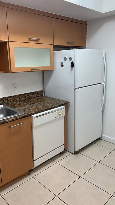 Kitchen featuring wood cabinetry with glass-panel upper door, stone-surface countertops, stainless steel sink, and tile flooring