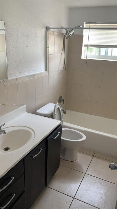 Bathroom featuring a dark-toned vanity cabinet with a light-toned solid surface countertop, an integrated oval sink, a wall-mounted faucet, and square ceramic wall and floor tiles