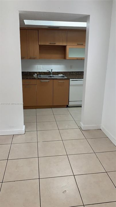 Kitchen featuring wood-finish cabinetry, natural stone countertops, dual-basin stainless steel sink, integrated dishwasher, and tiled flooring