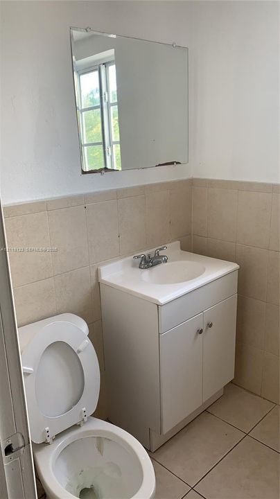 Bathroom featuring a vanity with an integrated sink, polished metal faucet, wall-mounted mirror, ceramic wall tiling, and ceramic floor tiling