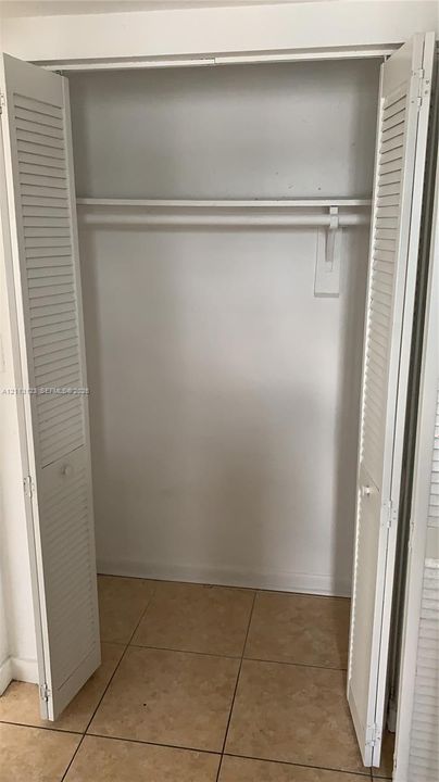 Reach-in closet featuring white louvered bi-fold doors, a fixed hanging rod, and ceramic tile flooring