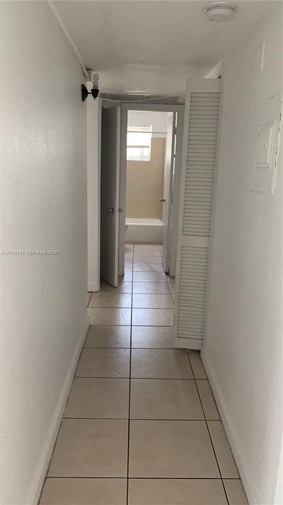 Hallway featuring neutral tile flooring, louvered closet doors, and recessed ceiling lighting