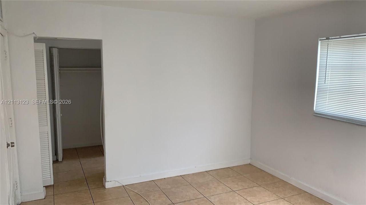 Neutral-toned room featuring tiled flooring, a louvered closet door, and a window equipped with horizontal blinds