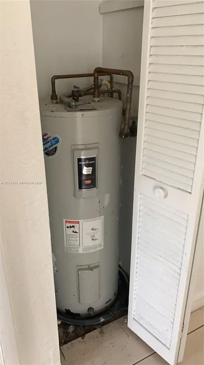 Utility closet featuring a water heater with copper plumbing connections and a white louvered door