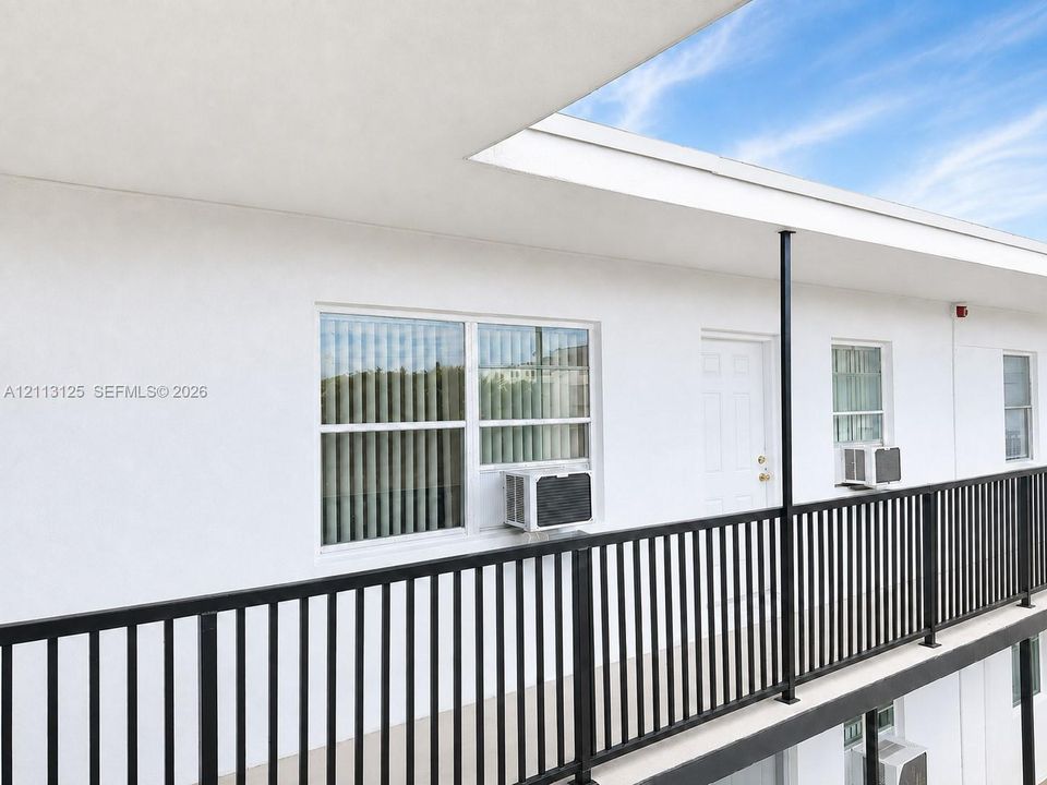 Exterior walkway featuring smooth white stucco siding, black metal railing, and white-framed multi-pane windows