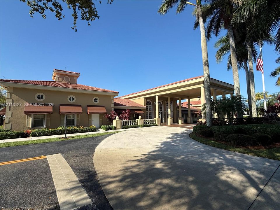 Exterior façade featuring a tile roof, covered porte-cochère, circular windows, stucco finish, and manicured landscaping