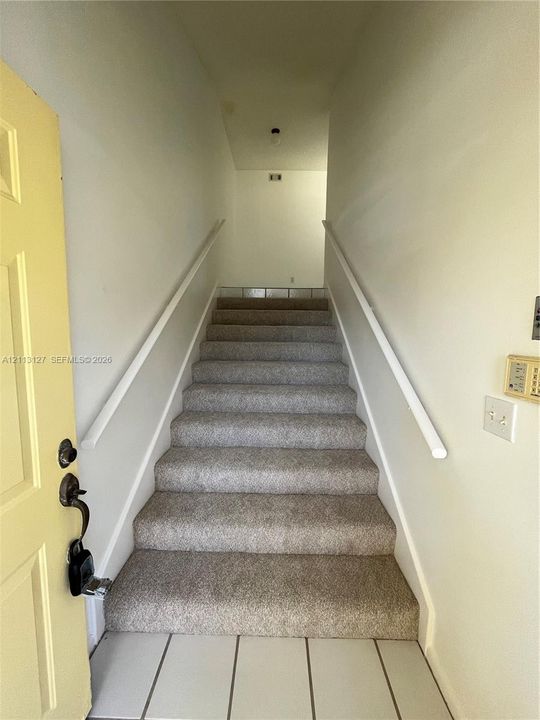 Staircase featuring wall-to-wall carpeting, dual white handrails, and a pale yellow entry door