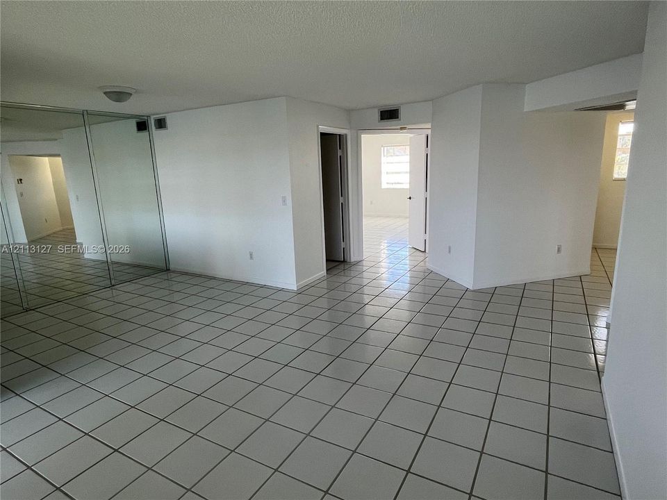 Open-concept interior featuring light-toned tile flooring, floor-to-ceiling mirrored closet doors, and multiple interior doorways