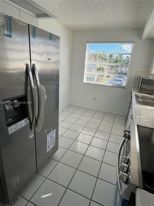 Kitchen featuring stainless steel side-by-side refrigerator, flat-surface electric range, double-basin stainless steel sink, tile flooring, and window with natural lighting