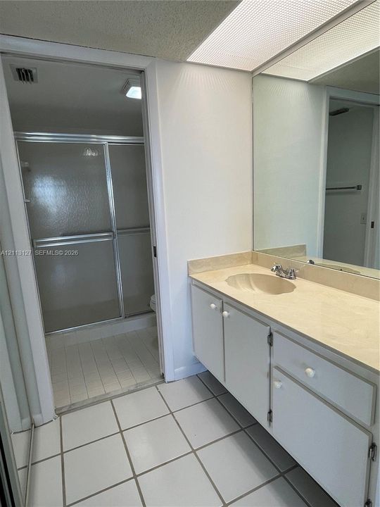 Bathroom featuring a vanity with an integrated sink, expansive wall-mounted mirror, tiled flooring, and a walk-in shower enclosure with sliding glass doors