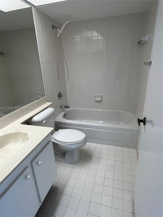 Bathroom featuring white tiled flooring, a shower-tub combination with white wall tile surround, a built-in vanity with an integrated sink, and a large wall-mounted mirror