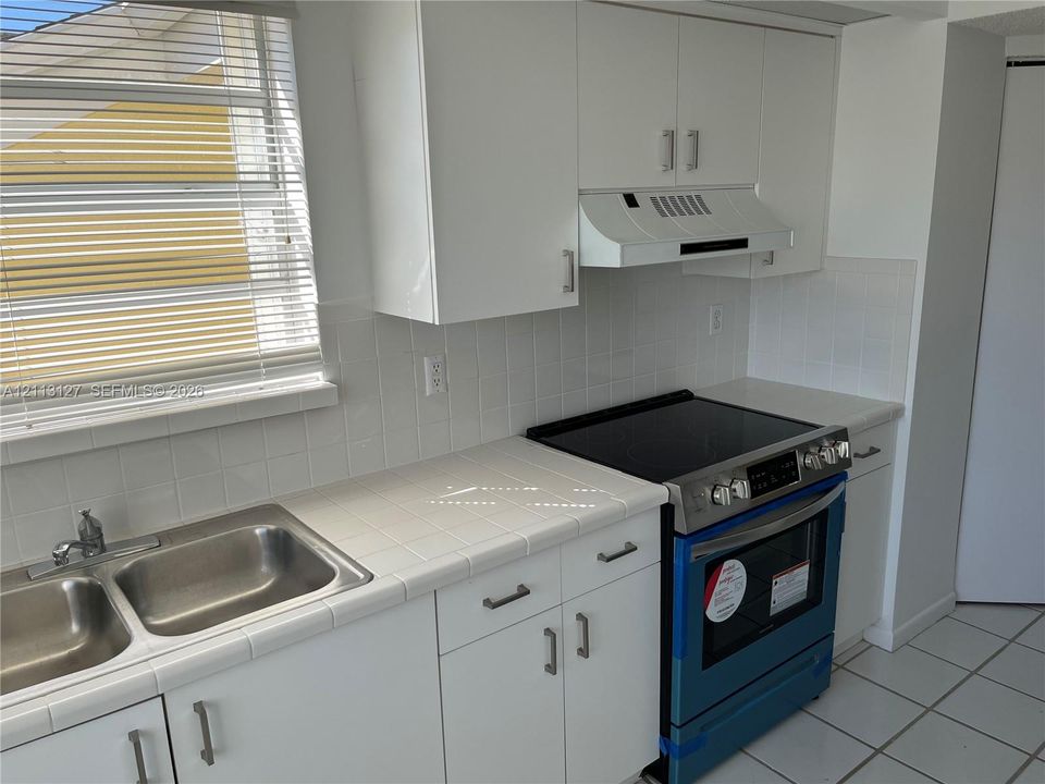 Kitchen featuring white cabinetry, tile countertops, tile backsplash, a double-basin stainless steel sink, and a slide-in electric range with integrated vent hood