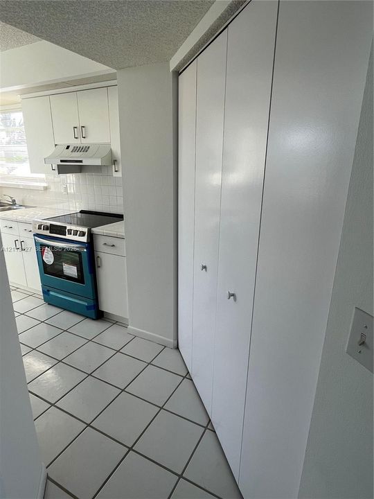 Kitchen featuring white shaker-style cabinetry, tiled flooring, tiled backsplash, and floor-to-ceiling bi-fold closet doors