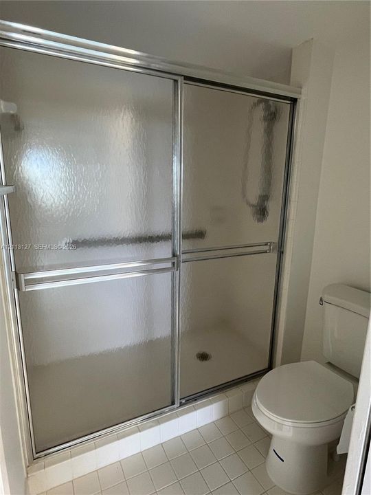 Shower enclosure featuring textured glass sliding doors with a metal frame and a ceramic tile floor