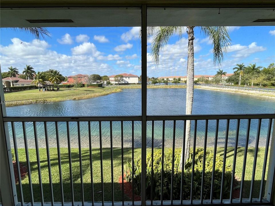 Screened-in enclosure with metal railings, overlooking a lake, manicured lawn, and mature palm trees