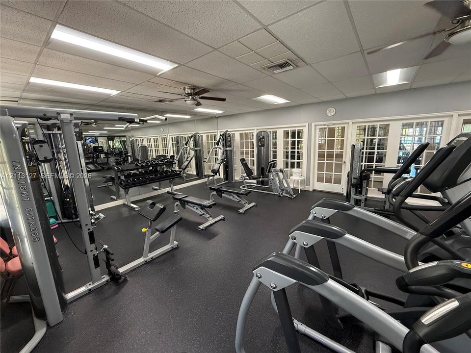 Fitness room featuring rubberized flooring, expansive wall-to-wall mirrors, recessed lighting, and multiple paneled glass doors
