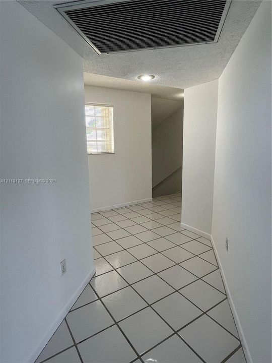 Hallway featuring square tile flooring with contrasting grout, neutral wall finishes, a recessed ceiling light, and a window with a grid pattern