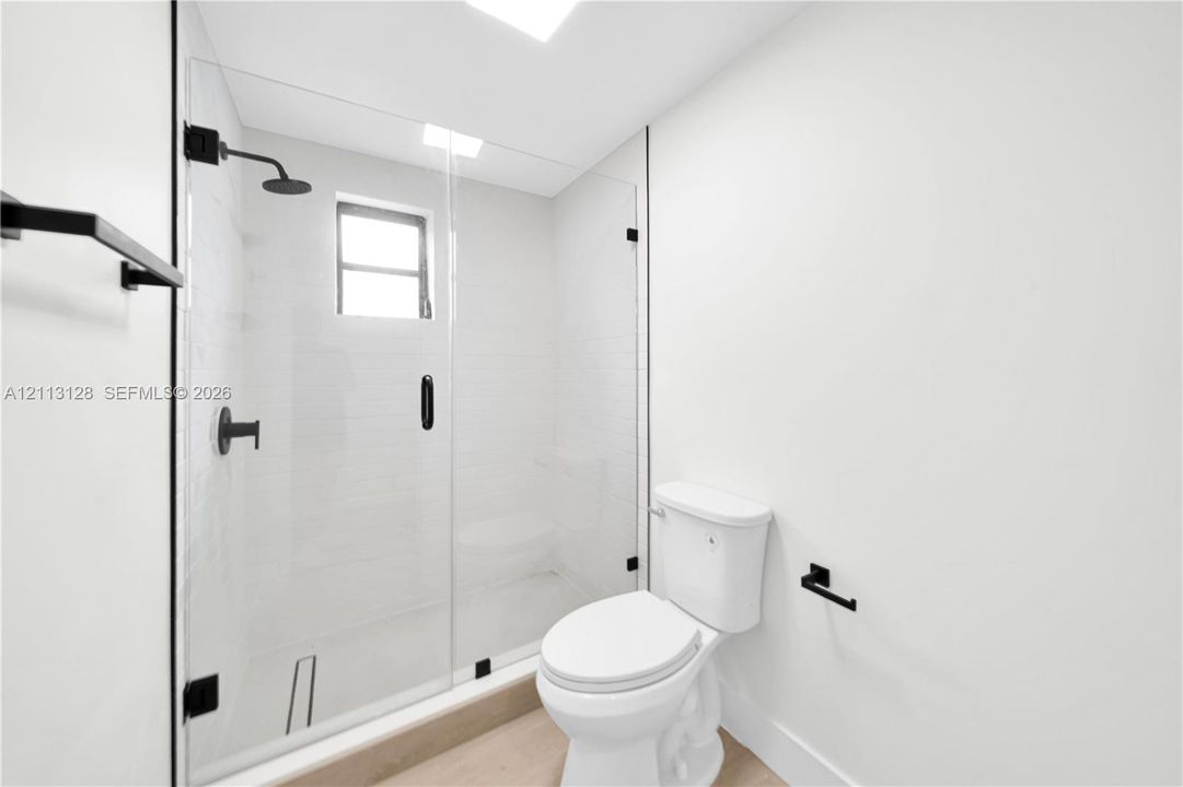 Walk-in shower featuring a frameless glass enclosure, matte black fixtures, rainfall showerhead, and white subway tile surround, finished with wood-finish flooring
