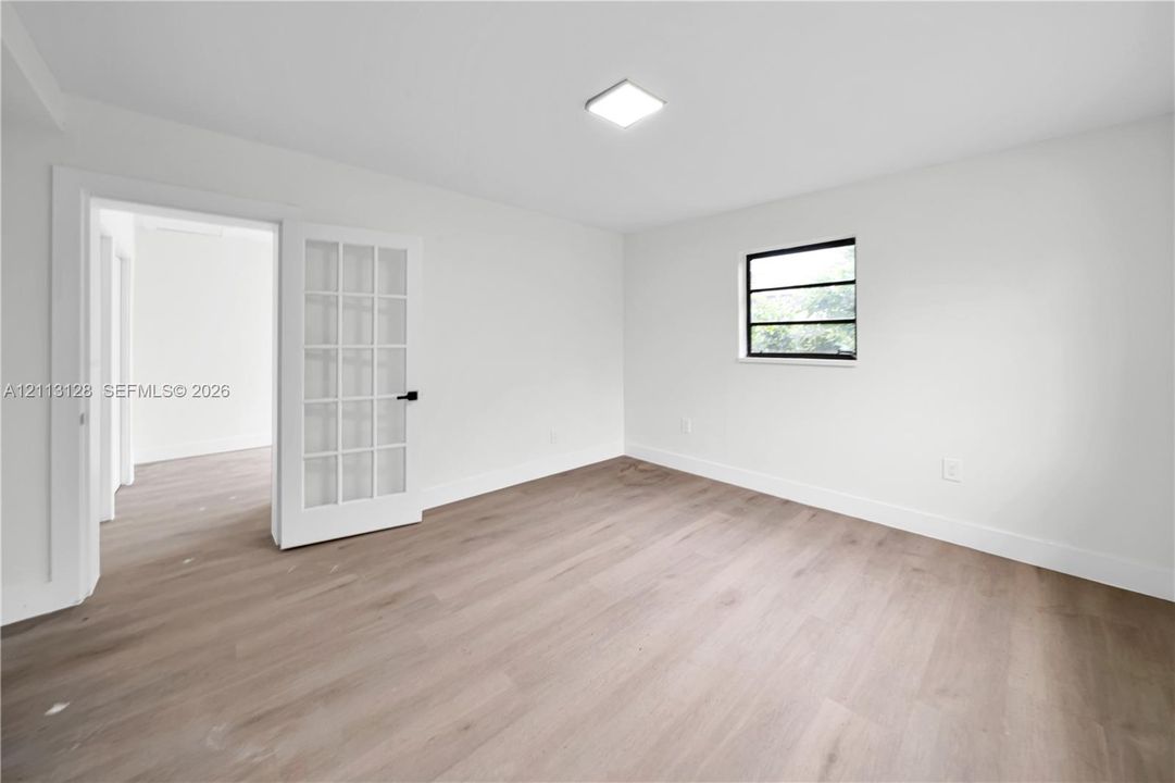 Room featuring wood-finish flooring, white walls, a multi-pane French door, a single-pane window with black framing, and a flush-mount ceiling light fixture