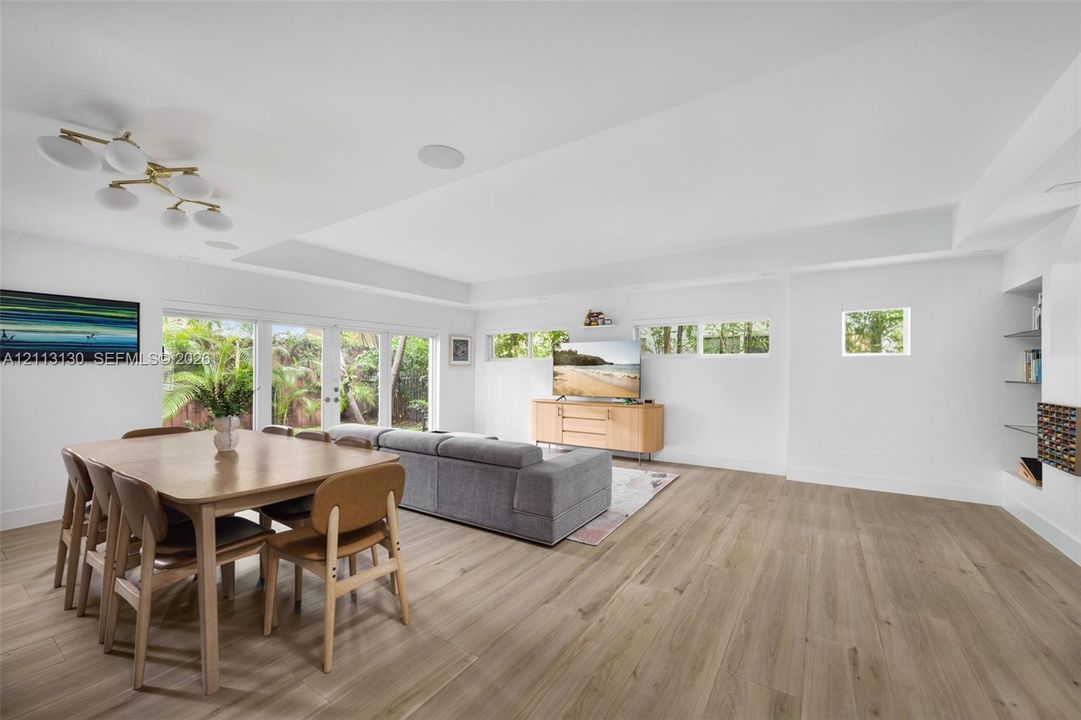 Open-concept interior featuring wood-finish flooring, recessed lighting, multi-panel glass exterior doors, clerestory windows, and built-in glass shelving