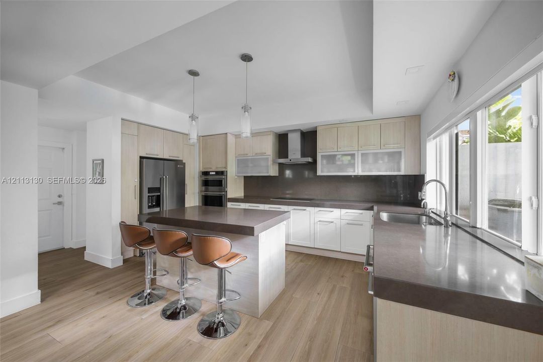 Kitchen featuring wood-finish cabinetry, stone countertops, stainless steel appliances, double wall ovens, and dual pendant lighting