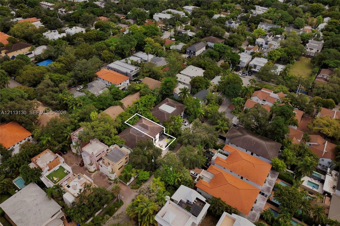 Aerial perspective showcasing a residential property with a hip roof, integrated hardscaping, and surrounding mature tree canopy
