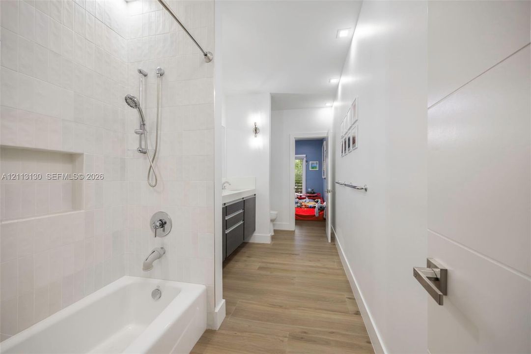 Bathroom featuring a soaking tub with integrated shower head, tiled wall surround with built-in niche, wood-finish flooring, floating dual-drawer vanity, and recessed lighting