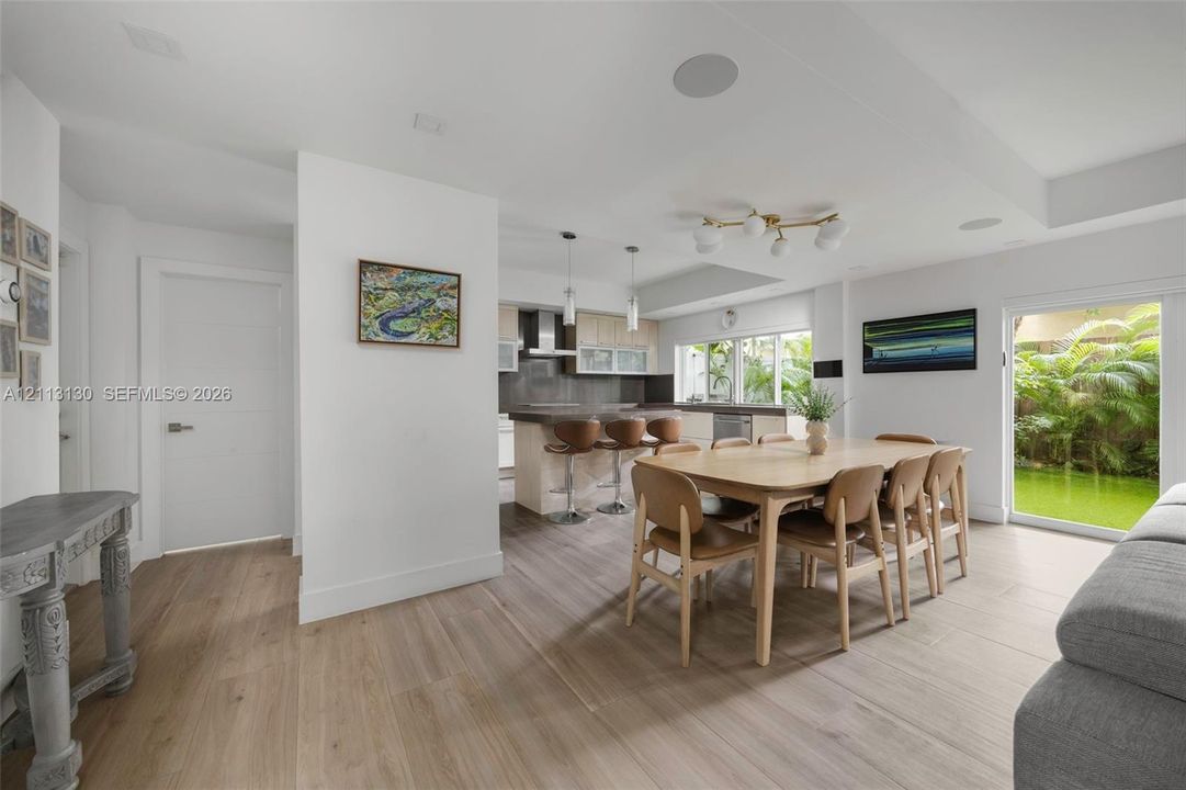 Open-concept interior featuring light wood-finish flooring, kitchen island with stone countertop, recessed ceiling speakers, modern multi-globe chandelier, and sliding glass door