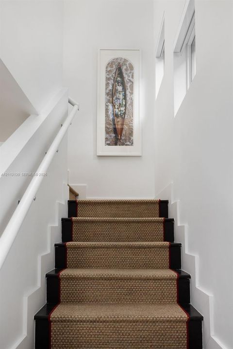 Staircase featuring dark-finished wooden treads, textured stair runner with a bordered edge, white wall-mounted handrail, and high-reaching walls with geometric moulding
