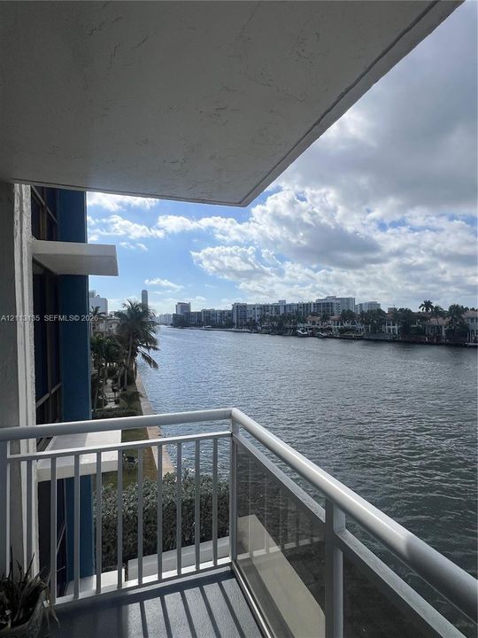 Covered balcony featuring white metal railings and concrete flooring overlooking a waterfront canal