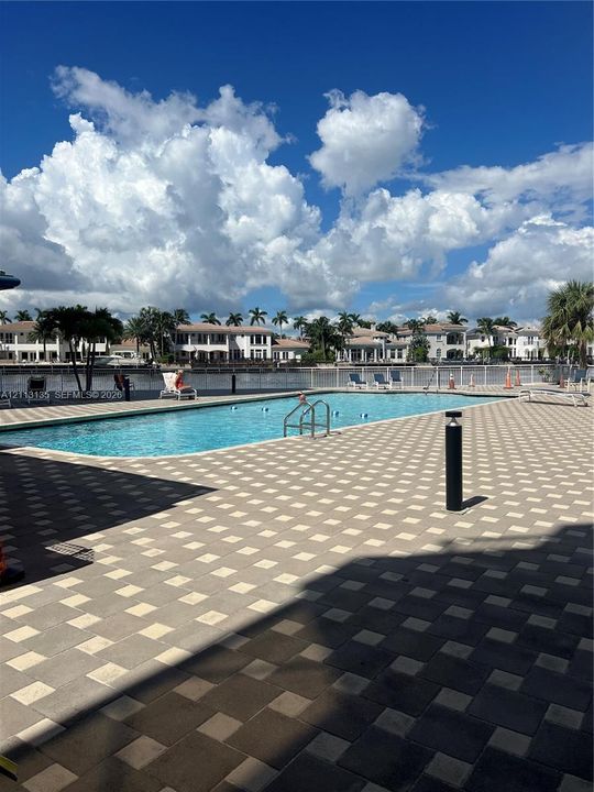 In-ground swimming pool featuring a geometric paver deck, metal safety fencing, and direct water frontage
