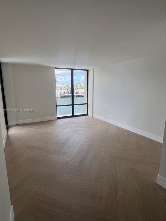 Herringbone wood-finish flooring, floor-to-ceiling windows with black metal frames, and water exposure