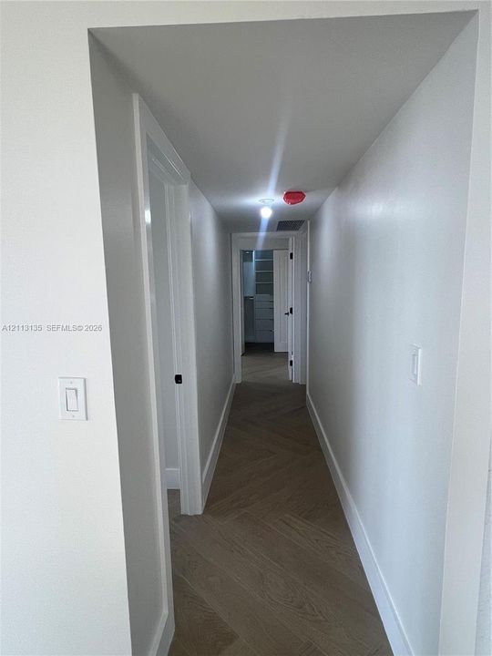 Hallway featuring herringbone-pattern wood-finish flooring, white walls, and interior passage doors