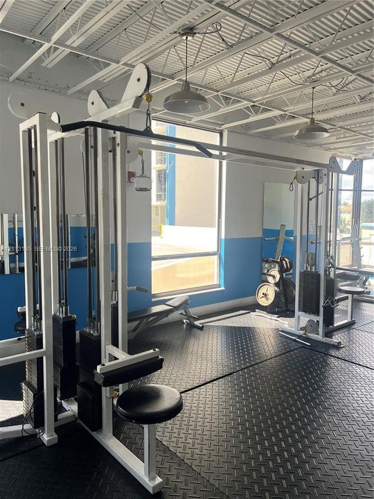 Fitness facility featuring high, exposed-joist ceilings, industrial-style pendant lighting, rubberized diamond-plate flooring, and large windows