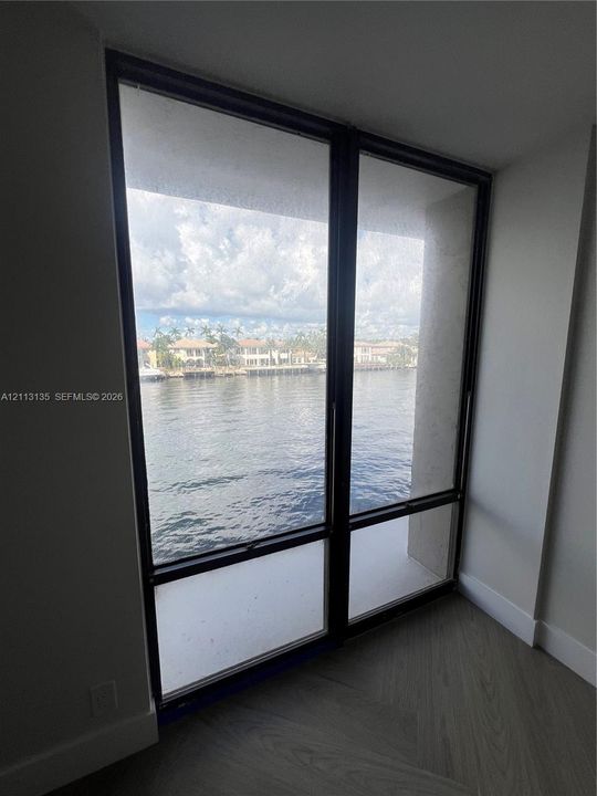 Floor-to-ceiling windows with dark metal frames, wood-finish flooring, and expansive water exposure