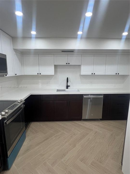 Kitchen featuring two-tone cabinetry, solid surface countertops, a matte black faucet, integrated stainless steel appliances, and herringbone-pattern wood-finish flooring