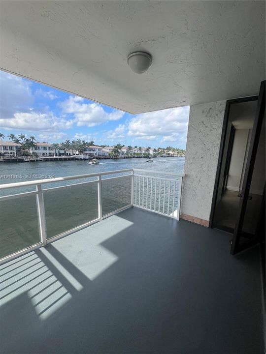 Covered balcony featuring water frontage, white metal railing, solid flooring, and textured wall finish
